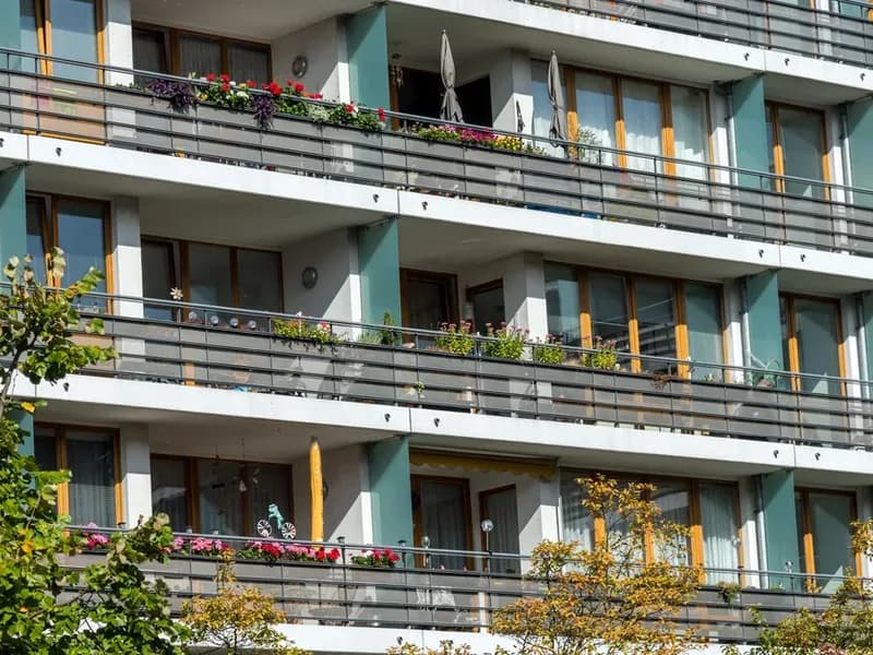 Průčelí bytového domu s řadami balkonů, na zábradlí truhlíky s květinami