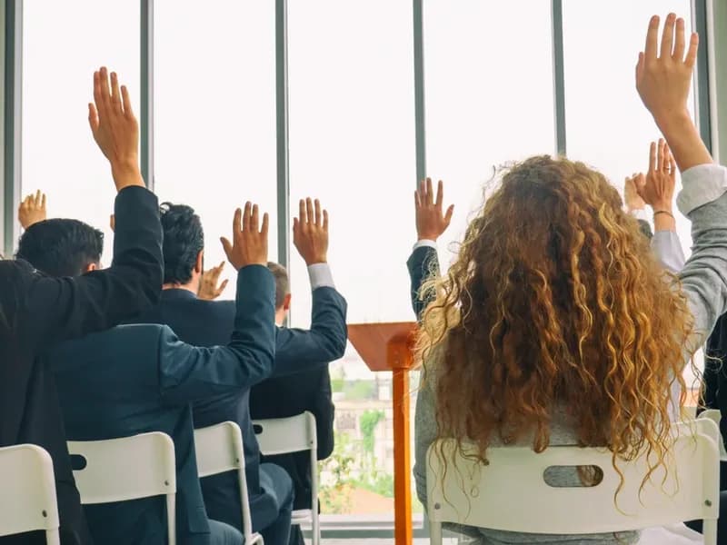 Vlastníci sedící v řadách na shromáždění SVJ zvedají ruku při hlasování